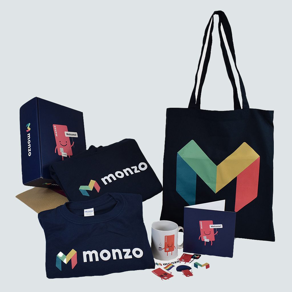 Collection of Monzo branded merchandise t shirt, bag, mug, stickers, printed box